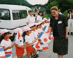 沿道に幼稚園児が日本とフランスの国旗を両手に持ち、笑顔でセリエール村から代表団の方を歓迎している様子の写真